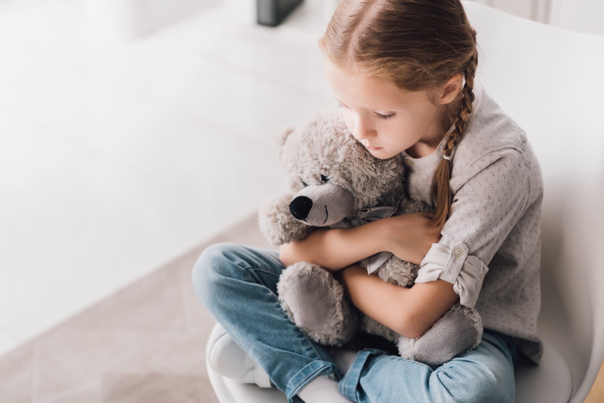 high angle view of depressed little child embracing her teddy bear